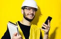 Studio portrait of young smiling man architect, builder engineer, wearing white construction safety helmet, glasses and jacket.