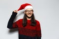 Studio portrait of young smiling man with long hair and eyeglasses, wears red Christmas sweater, holding pompon of Santa hat on a Royalty Free Stock Photo