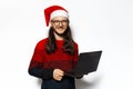 Studio portrait of young smiling man in red sweater, holding laptop, wearing Santa Claus hat and eyeglasses. Isolated on white. Royalty Free Stock Photo