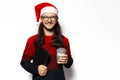 Studio portrait of young smiling man in red sweater, wearing Santa Claus hat and eyeglasses, holding laptop and mug of coffee. Royalty Free Stock Photo