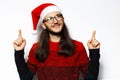 Studio portrait of young smiling man in red sweater, wearing Santa Claus hat and eyeglasses, pointing fingers up, looking up. Royalty Free Stock Photo