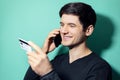 Studio portrait of young smiling man talking on smartphone and looking at his credit card in hand on background of aqua menthe. Royalty Free Stock Photo