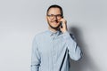 Studio portrait of young smiling man talking on smartphone, wearing eyeglasses and blue shirt on grey background Royalty Free Stock Photo