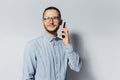 Studio portrait of young smiling man talking on smartphone, wearing eyeglasses and blue shirt on white background Royalty Free Stock Photo