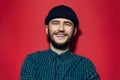 Studio portrait of young smiling man wearing black beanie hat and green plaid shirt on red background. Royalty Free Stock Photo