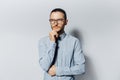 Studio portrait of young thoughtful man in blue shirt wearing eyeglasses, touching his chin on white background Royalty Free Stock Photo