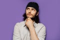 Studio portrait of young thoughtful man, with long dark hair, on the background of purple wall. Minding some good ideas.