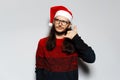 Studio portrait of young thoughtful  man with long hair and eyeglasses, doing phone gesture with hand, wears red Christmas sweater Royalty Free Stock Photo