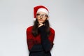 Studio portrait of young thoughtful man with long hair and eyeglasses, wears red Christmas sweater and Santa hat on a white Royalty Free Stock Photo