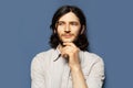 Studio portrait of young thoughtful man with long hair looking away. Background of blue color. Royalty Free Stock Photo