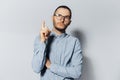 Studio portrait of young thoughtful man pointing index finger up, looking up, on white background. Wearing eyeglasses and blue Royalty Free Stock Photo