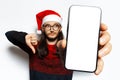 Studio portrait of young thoughtful man in red sweater, holding big smartphone with blank on screen, showing thumbs down, wearing Royalty Free Stock Photo