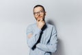 Studio portrait of young thoughtful man touches chin, looking up, on white background. Wearing eyeglasses and blue shirt. New idea Royalty Free Stock Photo