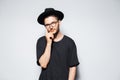 Studio portrait of young thoughtful man wearing black shirt, hat and eyeglasses. Royalty Free Stock Photo