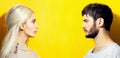 Studio profile portrait of couple, blonde girl and brunette guy looking each other on yellow background with copy space. Royalty Free Stock Photo