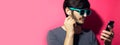 Studio profile portrait of serious young man looking in smartphone, using wireless earphones, wearing cyan sunglasses on pink back Royalty Free Stock Photo