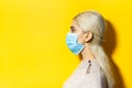 Studio profile portrait of young blonde girl, wearing flu medical mask on yellow background with copy space. Royalty Free Stock Photo