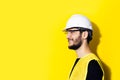 Studio profile portrait of young smiling man architect, builder engineer, wearing white construction safety helmet, glasses and ye