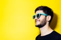 Studio profile portrait of young smiling man looking away, wearing cyan sunglasses on yellow background with copy space. Royalty Free Stock Photo