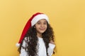 Studio shor of dark skinned young girl with long curly hair in a Santa Claus hat on a yellow background