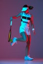 Studio shot of active professional tennis player training with tennis racket over gradient pink-purple background in