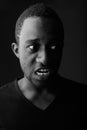 Studio shot of angry young black African man screaming in dark room Royalty Free Stock Photo