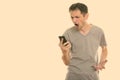 Studio shot of angry young man shouting while using mobile phone Royalty Free Stock Photo