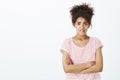 Studio shot of anxious cute dark-skinned woman in striped t-shirt, holding hands crossed on chest, frowning and