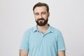 Studio shot of attractive adult bearded man, smiling and looking sincerely at camera, over gray background. Employee Royalty Free Stock Photo