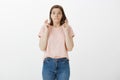 Studio shot of attractive emotive young european girl in pink t-shirt, biting lip and staring with popped eyes at camera