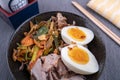 Studio shot of black bowl of ramen noodles with boiled eggs, veggies and turkey meet, ready to be poured with boiling