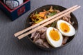 Studio shot of black bowl of ramen noodles with boiled eggs, veggies and turkey meet, ready to be poured with boiling