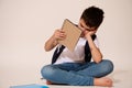 Studio shot of a bored upset demotivated schoolboy holding a copybook with free ad spacec, isolated on white background