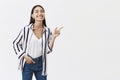 Studio shot of carefree emotive and friendly famous woman in stylish striped blouse, bending and pointing right with