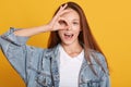 Studio shot of charming young woman, female making ok sign and covers her eye, posing with open mouth, expresses happyness, model