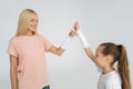 Studio shot of cheerful injured blonde young woman and little kid girl with broken hand wrapped in plaster bandage