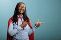 Studio shot of cheerful and optimistic justice defender woman wearing red cape while pointing fingers to right