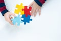 Close up and top view of autistic child`s hands holding and arranging colorful jigsaw puzzle on white table top background. Royalty Free Stock Photo