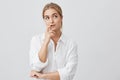 Studio shot of cunning beautiful woman with straight blonde hair looking aside holding hand under chin intending to Royalty Free Stock Photo