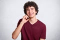 Studio shot of curly cheerful European male with little beard, curly hair, wearing casual dark red t shirt, isolated over white