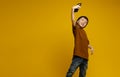 Studio shot of cute cheerful 6-year-old boy in a brown T-shirt, holding out his hand, holding a digital phone, taking a