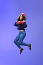 Studio shot of cute girl with curly hair in beanie sweatshirt and sneakers jumping playful and carefree over blue