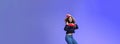 Studio shot of cute girl with curly hair in beanie sweatshirt and sneakers jumping playful and carefree over blue