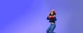 Studio shot of cute girl with curly hair in beanie sweatshirt and sneakers jumping playful and carefree over blue