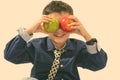 Studio shot of cute happy boy smiling while putting green and red apple on his eyes Royalty Free Stock Photo