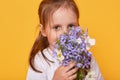 Studio shot of cute little girl wearing white shirt smelling bouquet of flower, present for her mummy, toddler wants to Royalty Free Stock Photo
