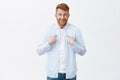 Studio shot of cute surprised businessman with ginger hair and bristle pointing at chest and chuckling, smirking from