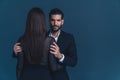 Studio shot on a dark blue background. Brunette long-haired woman standing back to camera, latin unshaved elegant man Royalty Free Stock Photo