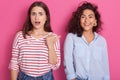 Studio shot of dark haired girls, adorable lady with open mouth points thumb at her smiling friend, females wear casual clothes, Royalty Free Stock Photo