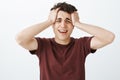 Studio shot of desperate crying caucasian man in red t-shirt, touching hair and screaming or whining, feeling miserable